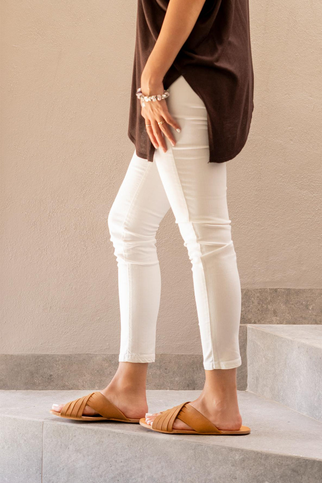 Martha Sandals in Tobacco worn with white jeans, side view standing on stone steps