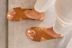 Martha Sandals in Tobacco worn with white pants, top-down view of feet on stone