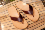 Pair of Flip Flops in Chestnut leather resting on a weathered wooden slatted table