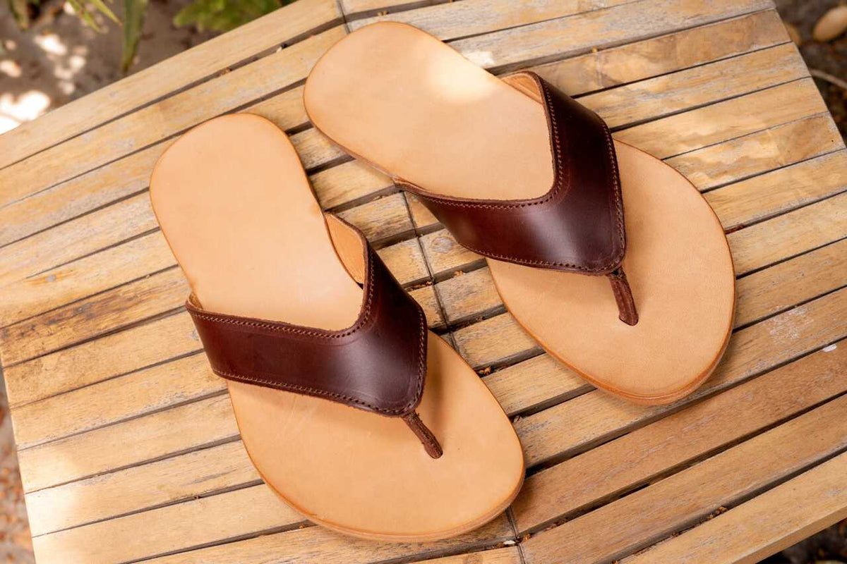 Pair of Flip Flops in Chestnut leather resting on a weathered wooden slatted table