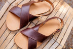 Pair of Jesus Sandals in Chestnut leather resting on a weathered wooden slatted bench