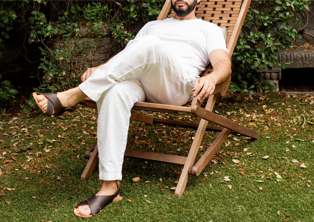 A man relaxing in a wooden lounge chair on the lawn wearing Jesus Sandals in Dark Coffee Brown