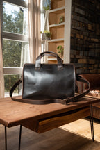 Simple Overnight Leather Duffle Bag in Dark Coffee Brown, sitting on a wooden table by a sunny window