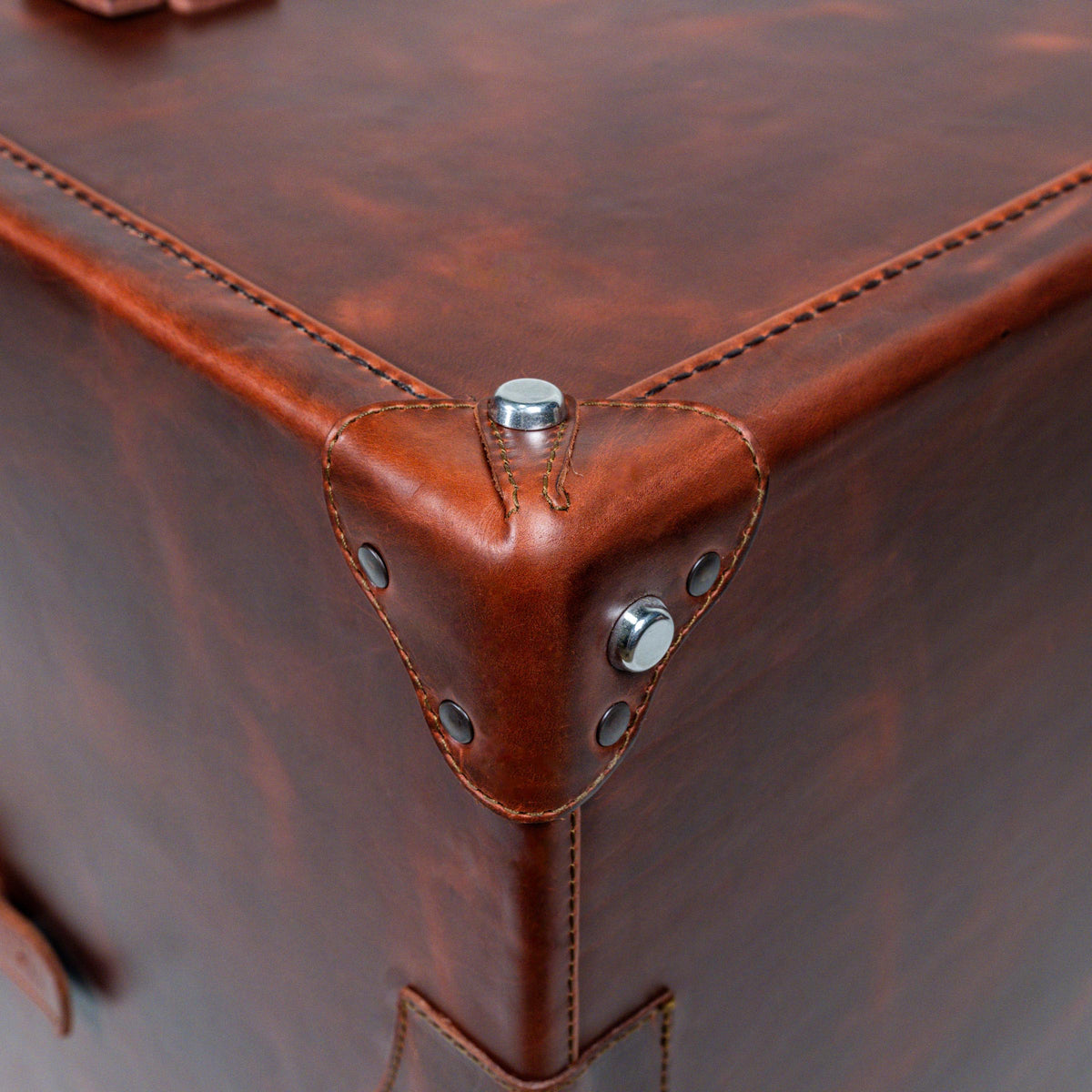Leather Small Trunk in Chestnut, close-up of stitched leather corner guard with metal rivets and studs