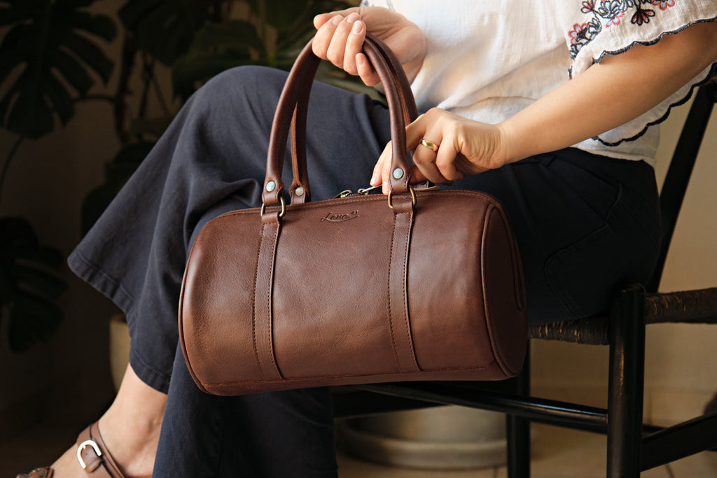 Everyday Barrel Bag in Chestnut, held on the lap by its top handles by a seated woman
