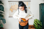 Leather Tumbled Fanny Bag in Tobacco, unzipped at the waist as a woman reaches inside