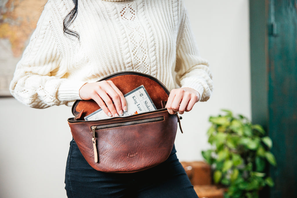 Leather Tumbled Fanny Bag in Chestnut, unzipped at the waist as a woman tucks cash inside