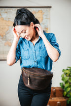 Leather Tumbled Fanny Bag in Dark Coffee Brown, worn at the hip by a smiling woman in front of a world map
