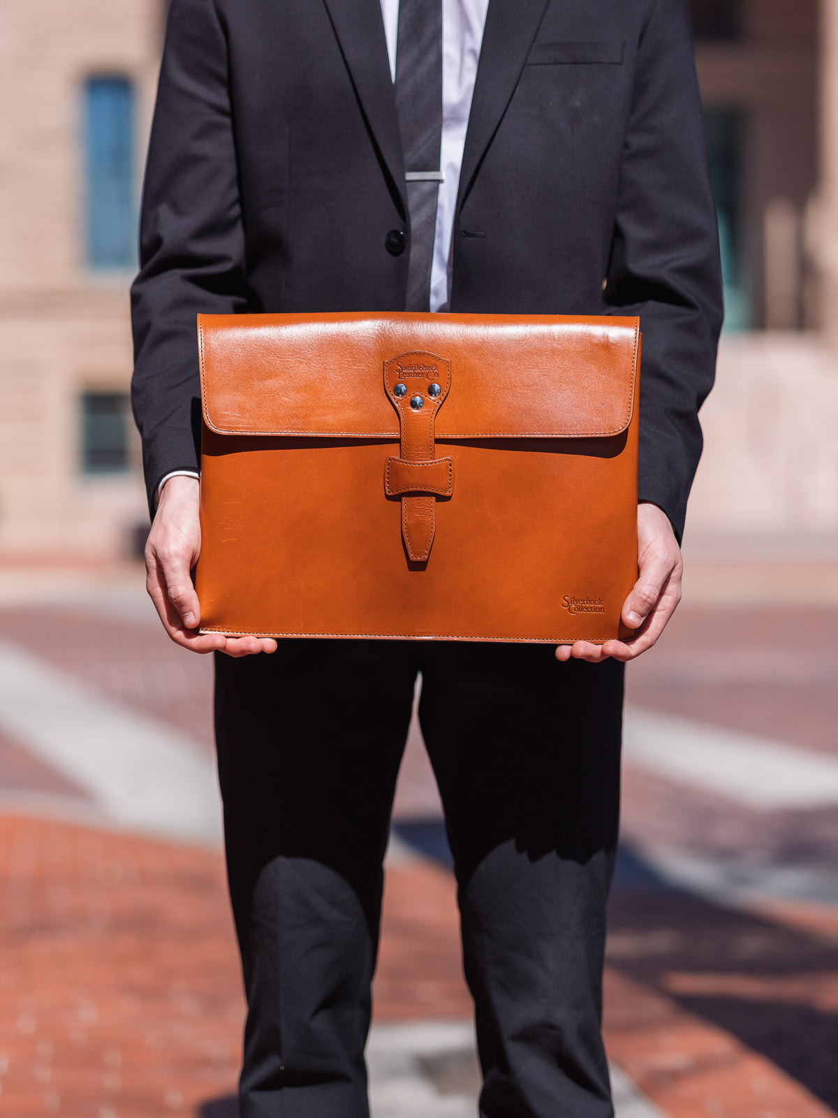 Silverback Document Holder in English Tan, held in front of a man in a dark suit outdoors