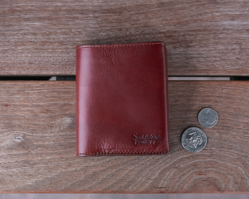 Large Bifold Wallet in Oxblood on a wooden table next to two coins for scale