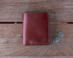 Large Bifold Wallet in Oxblood on a wooden table next to two coins for scale