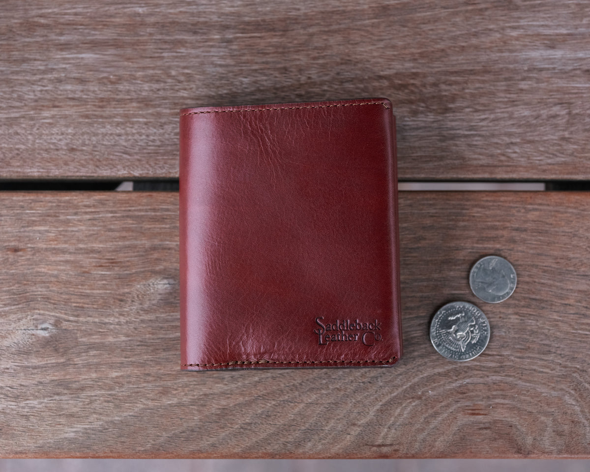 Large Bifold Wallet in Oxblood on a wooden table next to two coins for scale