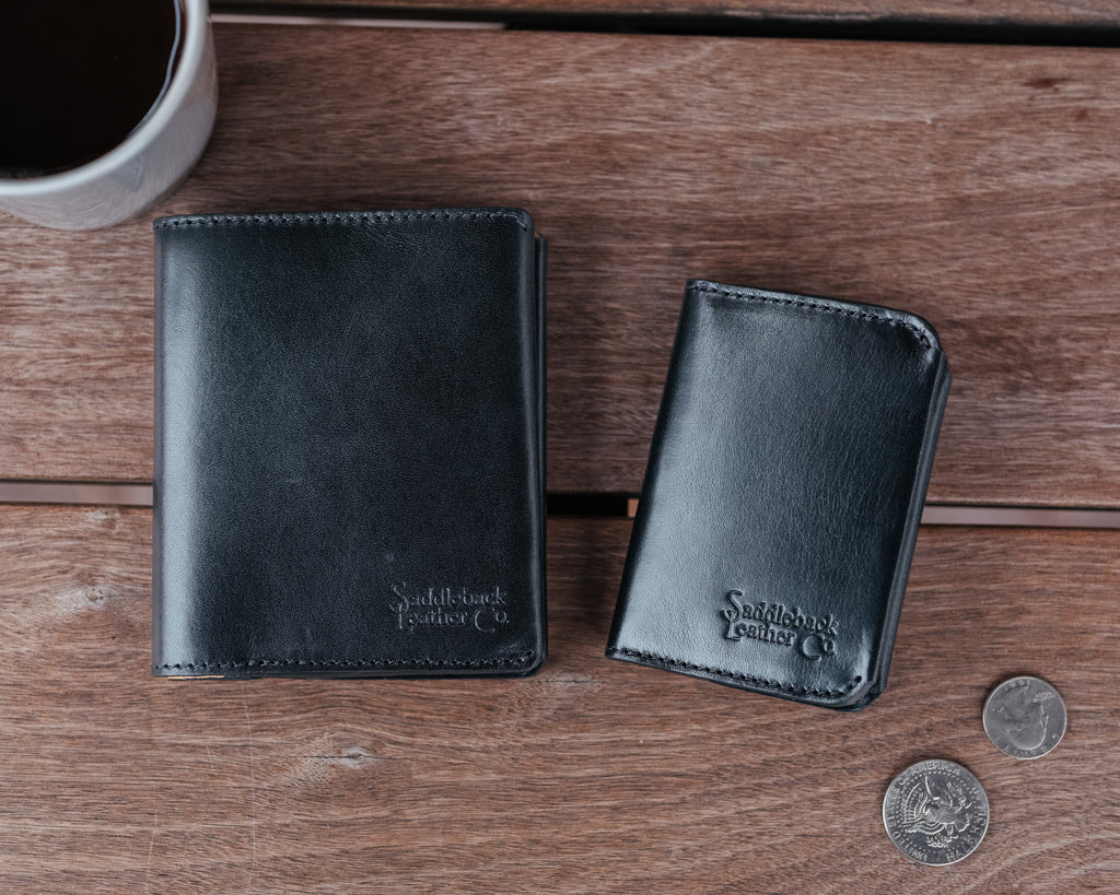 Large Bifold Wallet in Raven Black beside a smaller slim wallet on a wooden table with coins