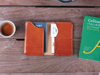 Wycliffe Passport Wallet in English Tan lying open with a passport and cards, beside a coffee cup and a dictionary