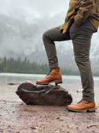 Huntsman Boots in Natural, one foot on a rock by a lake below misty mountains