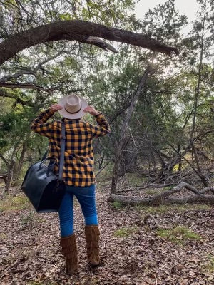 Simple Overnight Leather Duffle Bag carried on the shoulder by a person in a plaid shirt walking through the woods