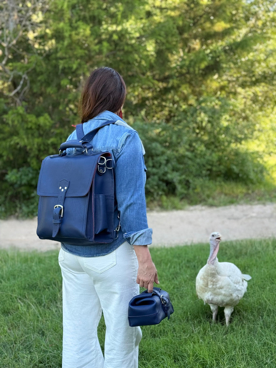 Saddleback Club Membership blue messenger bag backpack worn and toiletry bag carried outdoors near a white turkey