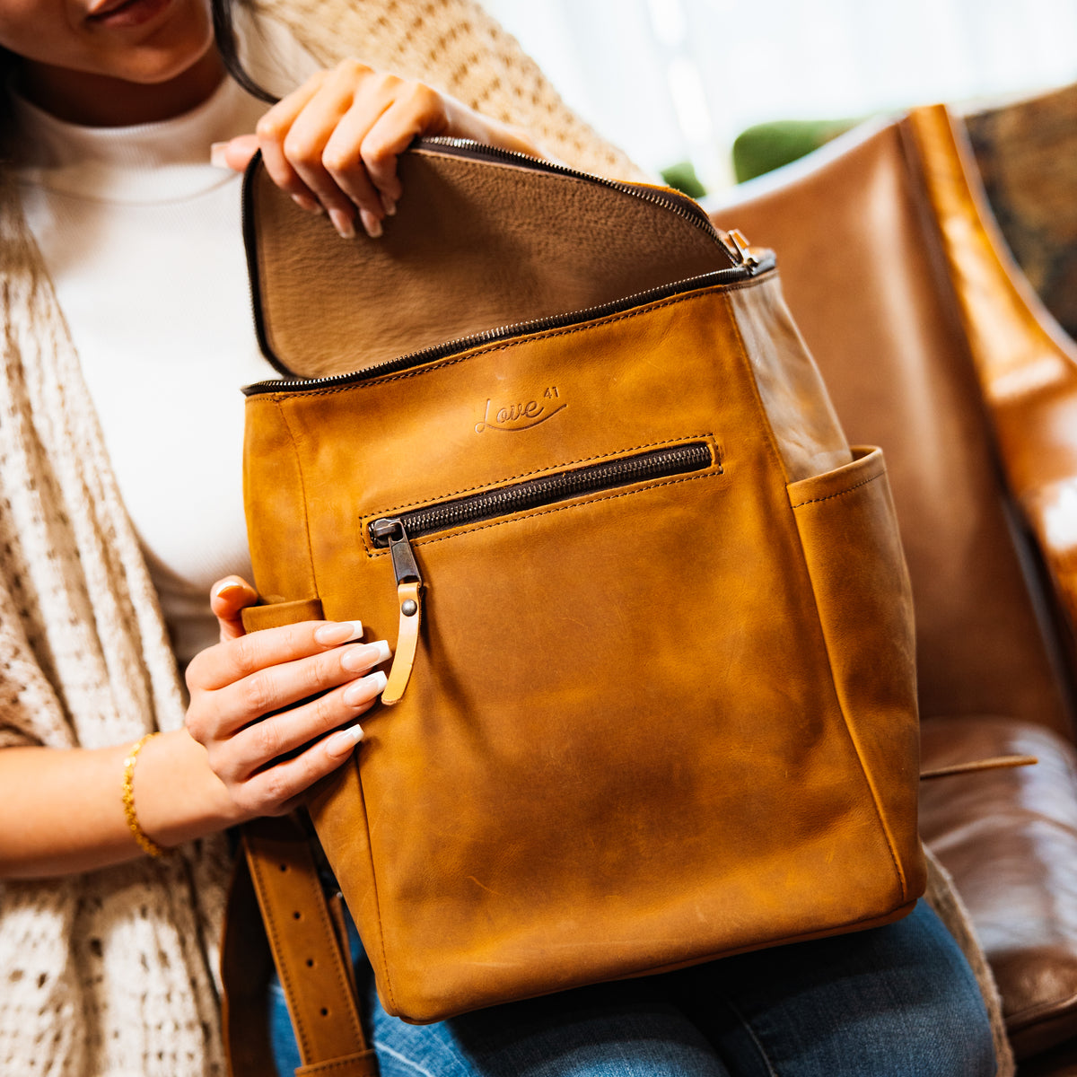 All in One Backpack Medium in Tobacco held on a lap while a woman unzips the top flap
