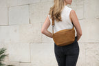 London Sling Small in Tobacco, worn crossbody at the back by a woman beside a pale stone wall