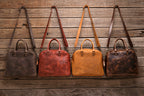 Professional Leather Satchel in Black, Chestnut, Tobacco and Dark Coffee Brown hanging side by side on a wood wall