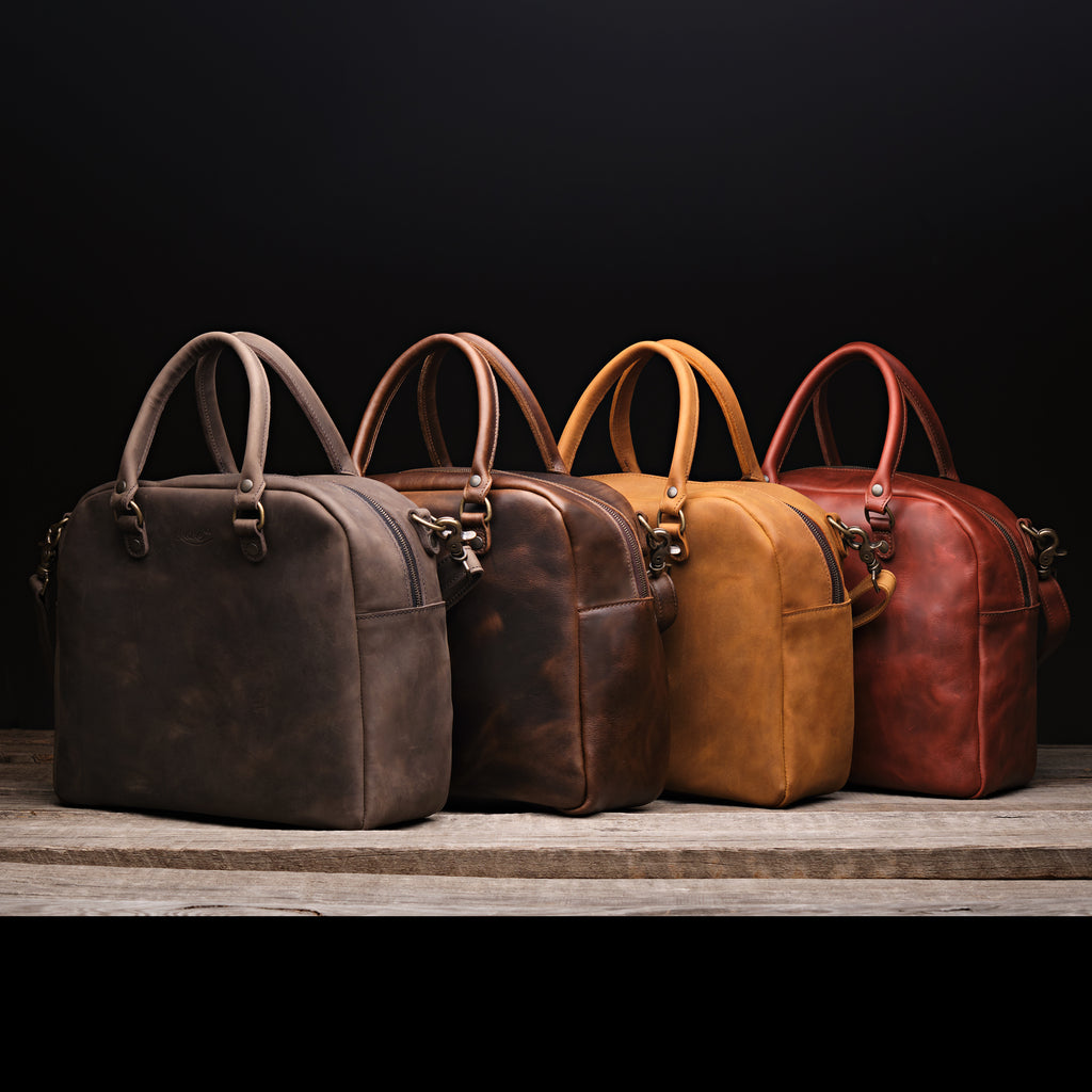 Professional Leather Satchel in Black, Dark Coffee Brown, Tobacco and Chestnut lined up in a row on a wood shelf