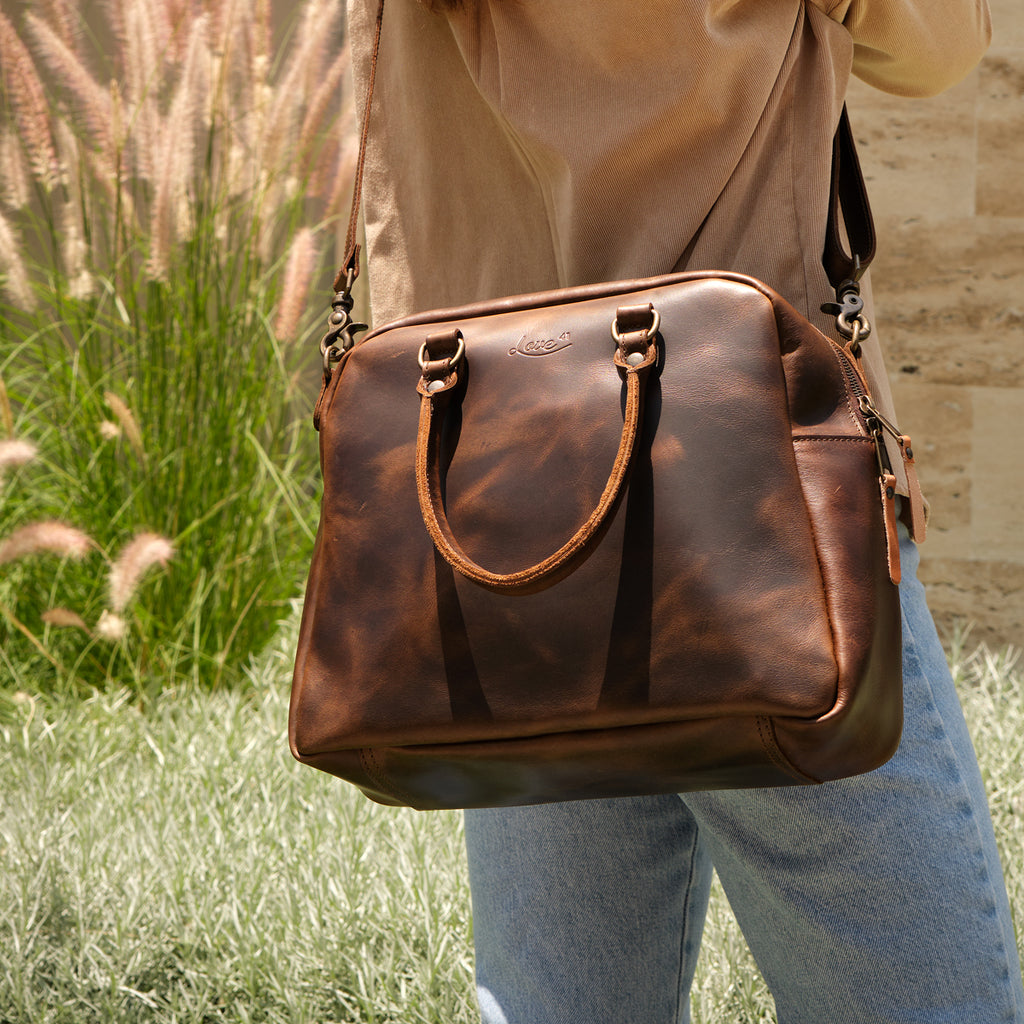 Professional Leather Satchel in Dark Coffee Brown, worn on the shoulder outdoors beside tall ornamental grass