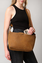 London Sling Large in Tobacco, worn crossbody while a woman slips a phone into the top