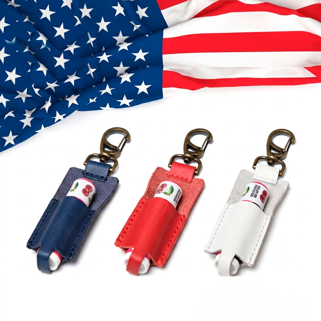 Leather lip balm holder keychains in navy blue, red and white with brass clips beneath an American flag