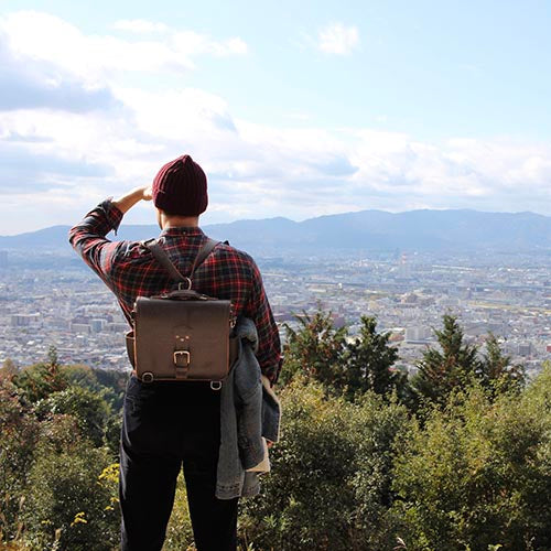 Photographer's Satchel in Dark Coffee Brown, worn as a backpack by a man overlooking a city