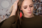 Leather Feather Earrings in Red worn by a woman in a brown sweater tucking back her hair