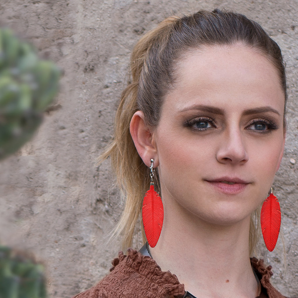 Leather Feather Earrings in Red worn by a woman with her hair in a ponytail against a stone wall
