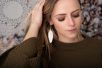 Leather Feather Earrings in White worn by a woman in a brown sweater tucking back her hair