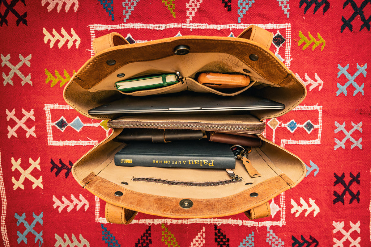 Leather Organizer Satchel in Tobacco, opened wide on a red patterned rug showing a laptop, books and pouches inside