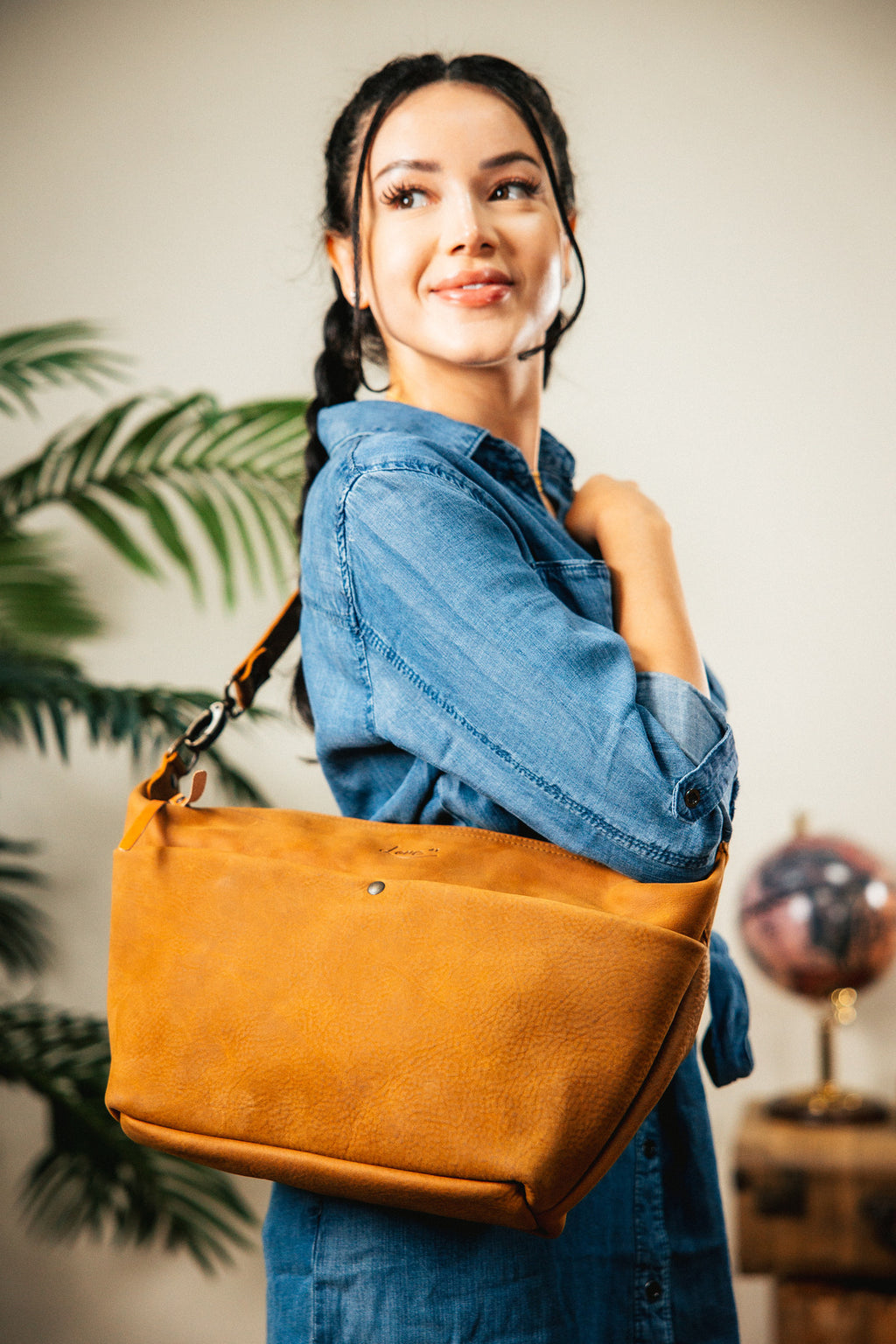 London Sling Large in Tobacco, carried on the shoulder by a smiling woman in a denim dress