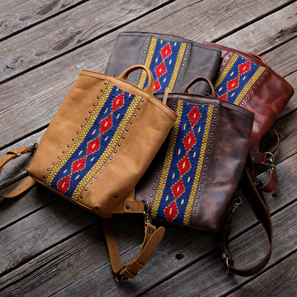 Lanita Leather Backpack in four colors laid on weathered wood, each with a blue and red woven panel