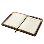 Medium Moleskin Cover in Dark Coffee Brown, open at an angle with a handwritten notebook and pen in the pen loop