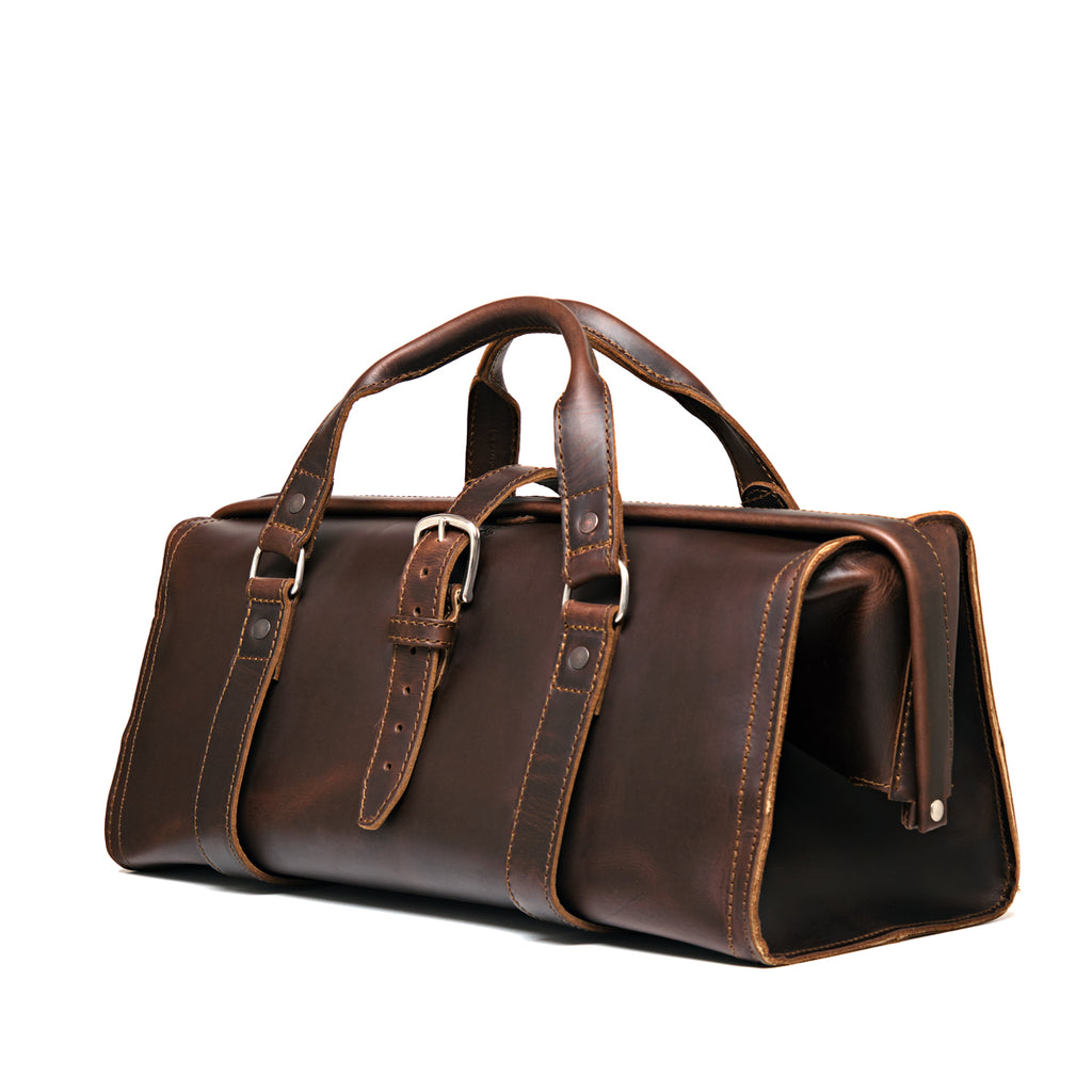 Leather Range and Tool Bag in Dark Coffee Brown, angled front view with top handles, buckle strap and side frame opening