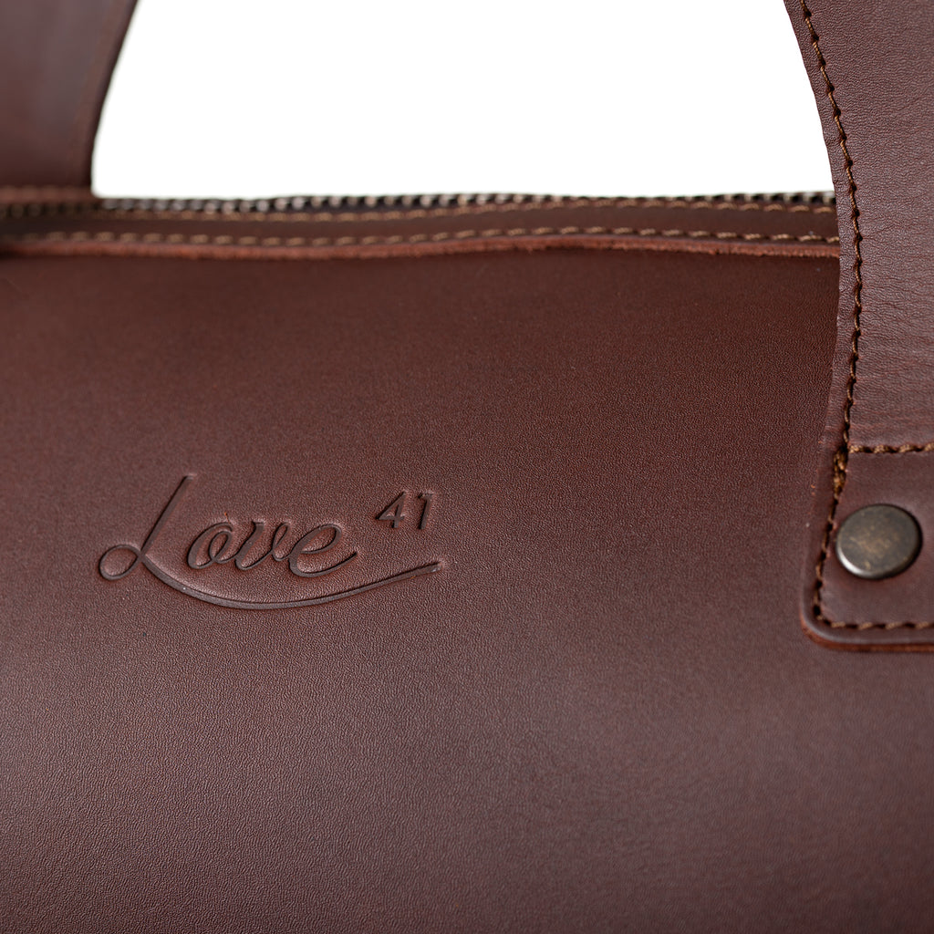 Simple Overnight Leather Duffle Bag in Chestnut, close-up of the embossed Love 41 logo and riveted handle