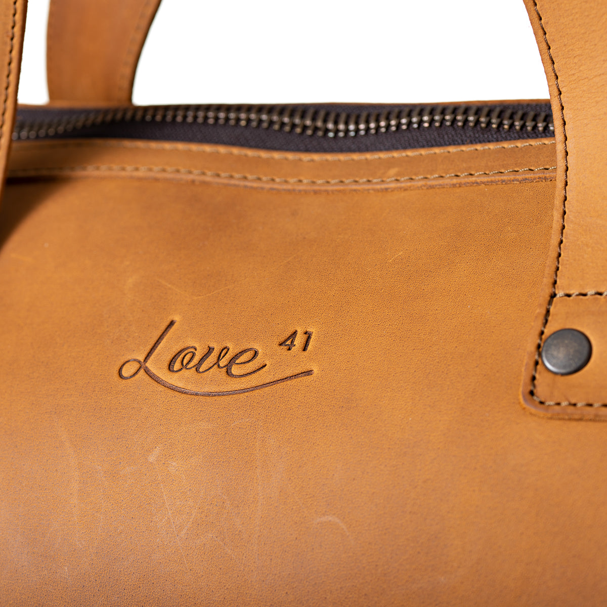 Simple Overnight Leather Duffle Bag in Tobacco, close-up of the embossed Love 41 logo and riveted handle