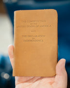 Pocket Declaration/Constitution in Tobacco held in one hand, embossed title on the cover