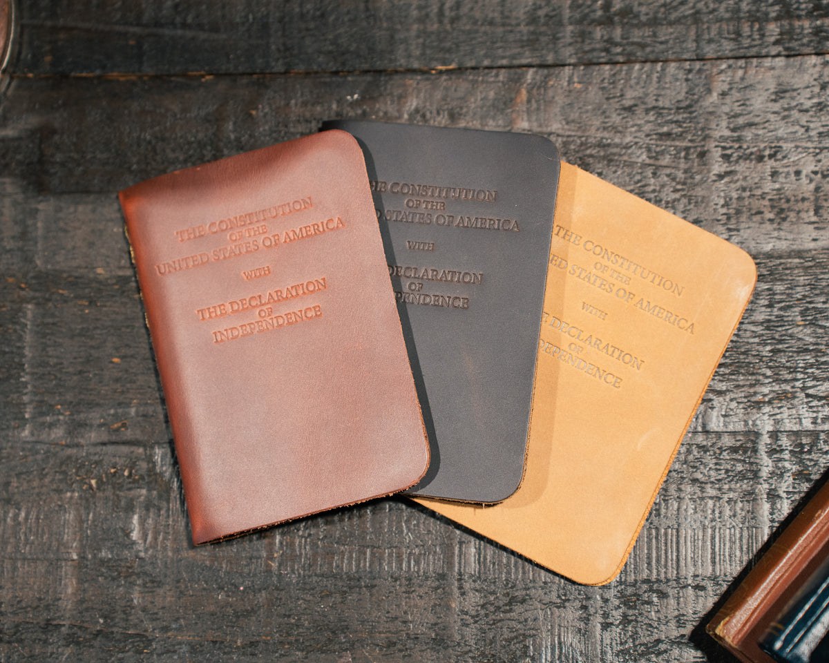 Pocket Declaration/Constitution in Chestnut, black and Tobacco fanned out on a dark wooden table
