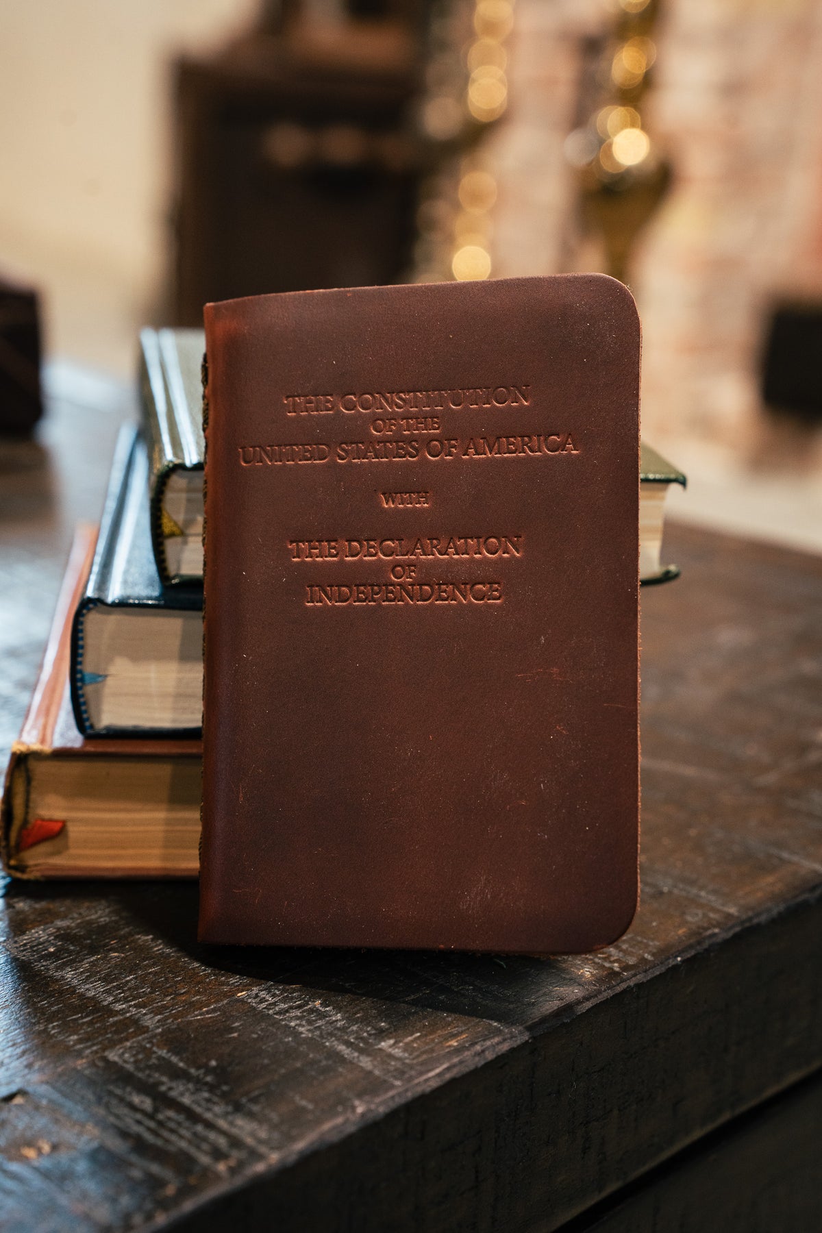 Pocket Declaration/Constitution in Dark Coffee Brown standing against a stack of books on a wooden table