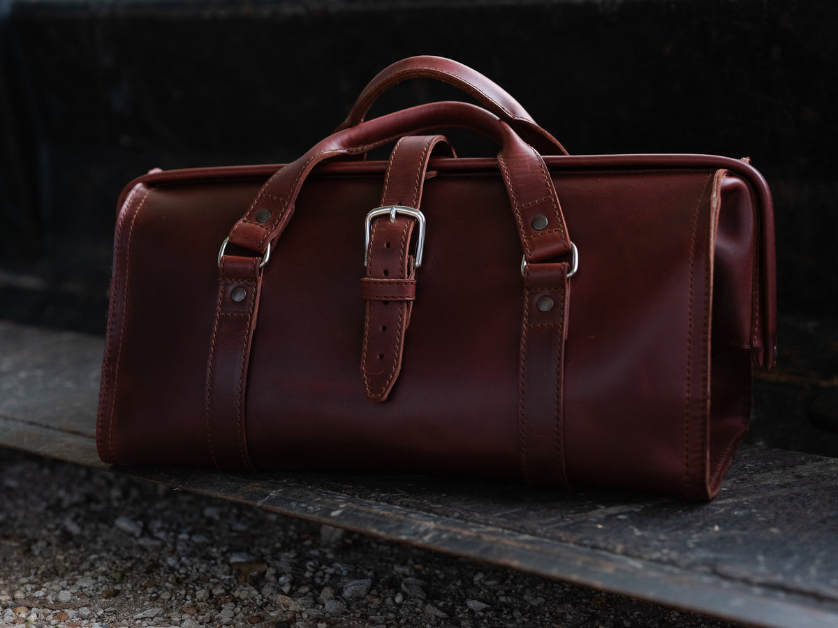 Leather Range and Tool Bag in Chestnut, front view on a dark wooden tailgate with top handles and buckle strap