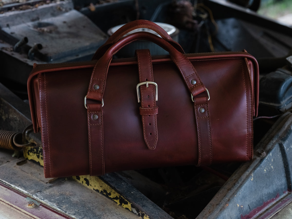 Leather Range and Tool Bag in Chestnut resting on old engine parts and rusted metal in a workshop