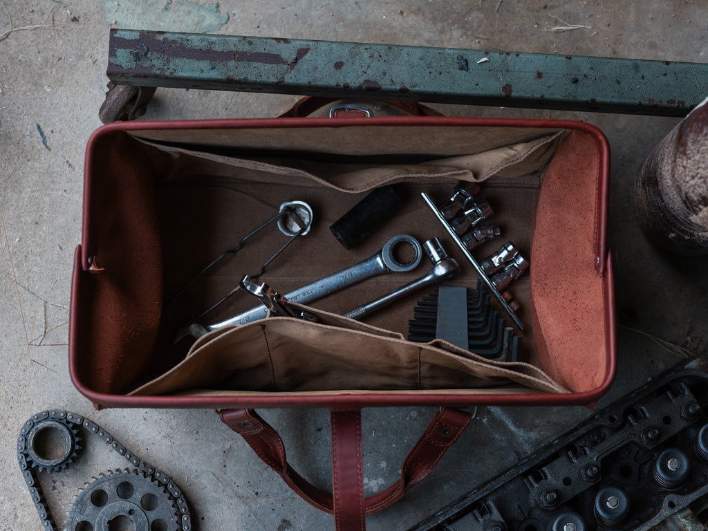 Leather Range and Tool Bag in Chestnut, top view open on a shop floor holding wrenches, sockets and hex keys