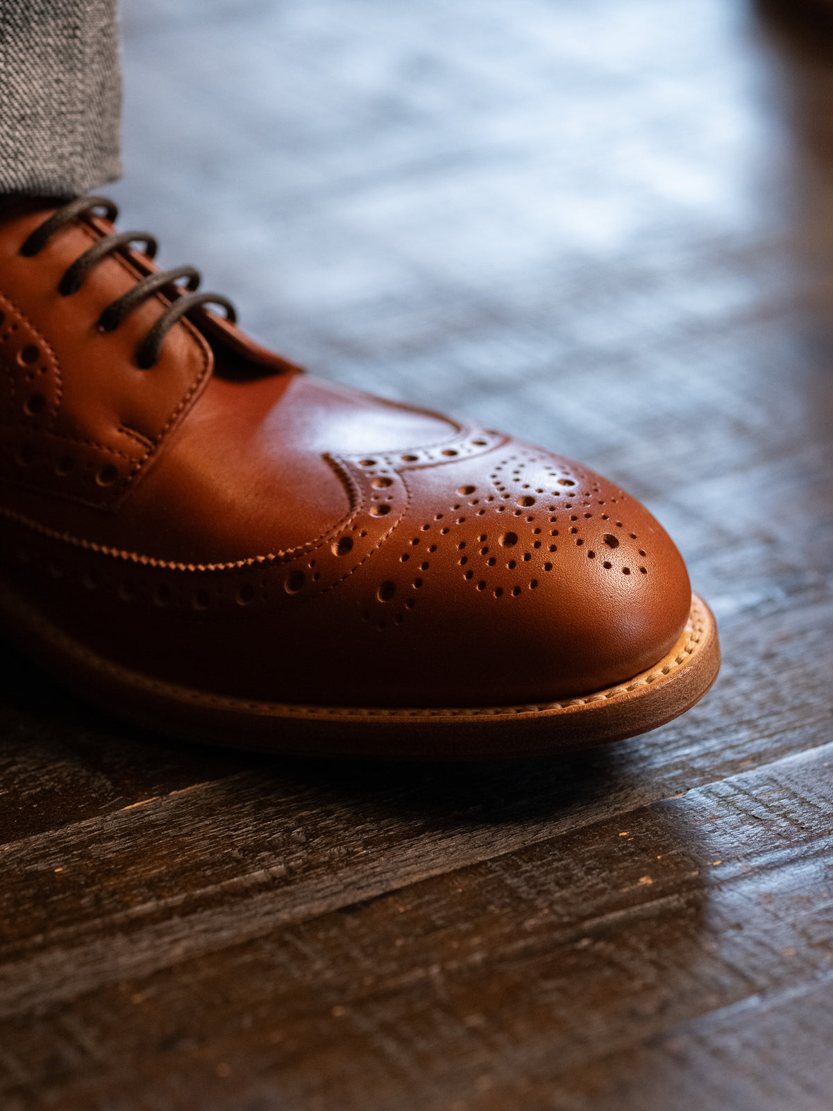 Wingtip Shoes in Natural Tan, close-up of brogue wingtip toe on a dark wooden floor