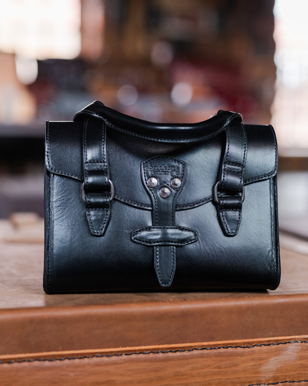 Double Handle Purse in Raven Black sitting on a wooden surface in a warmly lit room