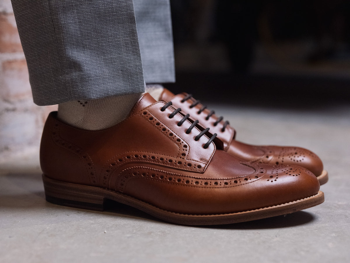 Wingtip Shoes in Natural Tan, side view worn with gray trousers on a concrete floor