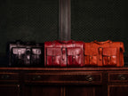 Blackstone Barrister Briefcase in Raven Black, Oxblood and English Tan lined up on a wooden sideboard