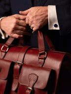 Blackstone Barrister Briefcase in Oxblood, close-up of hands gripping the top handles above the buckled pockets